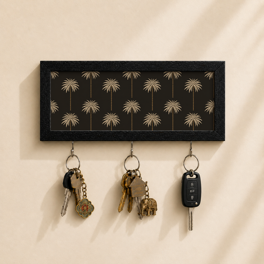A rectangular black wall-mounted key rack with a palm tree pattern, shown holding three sets of keys against a warm beige wall.