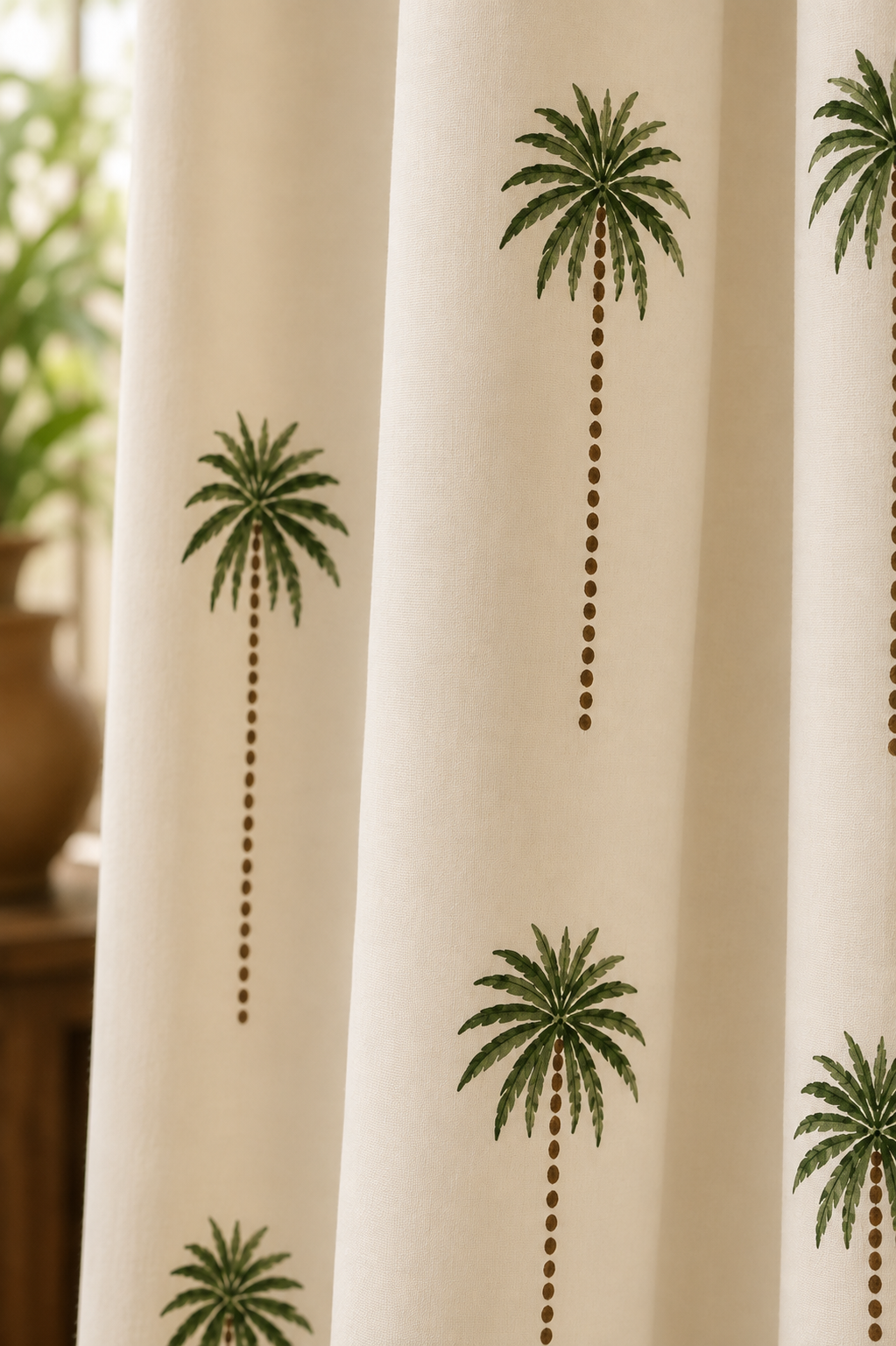 Off-white curtain panels featuring a repeating pattern of green palm trees with brown dotted trunks, shown hanging in a softly lit room.