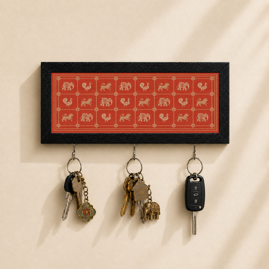 A rectangular black wall-mounted key holder with a red center panel featuring beige animal silhouettes, hanging three keys and a car key fob against a warm beige wall.
