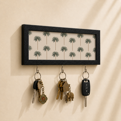 A rectangular black-framed wall hook with three hanging metal keys, shown mounted on a beige wall with warm sunlight and shadows.