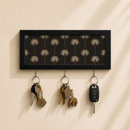 A rectangular black wall-mounted key rack with a palm tree pattern, shown holding three sets of keys against a warm beige wall.