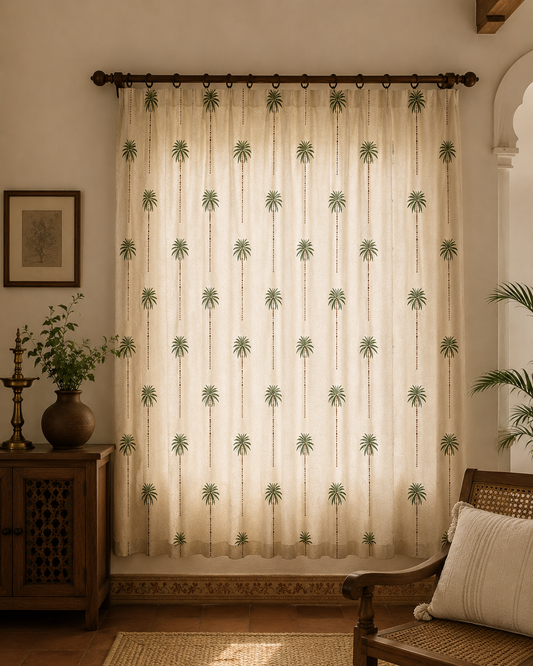 A long cream-colored curtain panel hanging on a dark rod in a warm, styled room. The curtain features a repeating vertical pattern of green palm tree silhouettes.