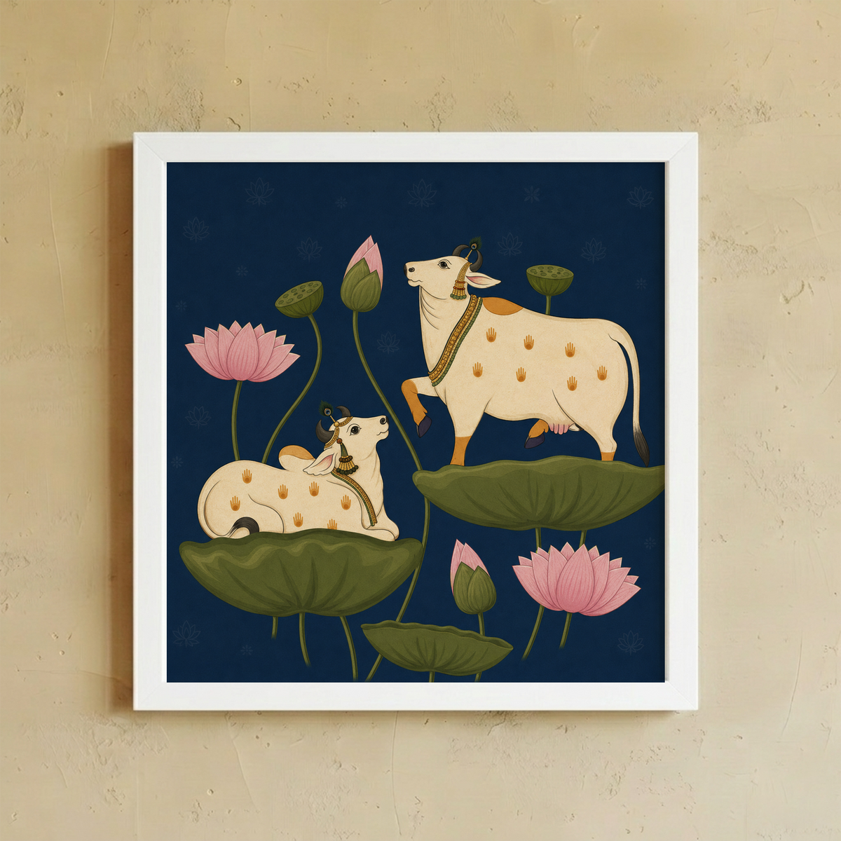 A framed art print featuring a stylized illustration of two cream-colored spotted cows among green lotus leaves and pink lotus flowers on a dark navy background, displayed on a textured beige wall.