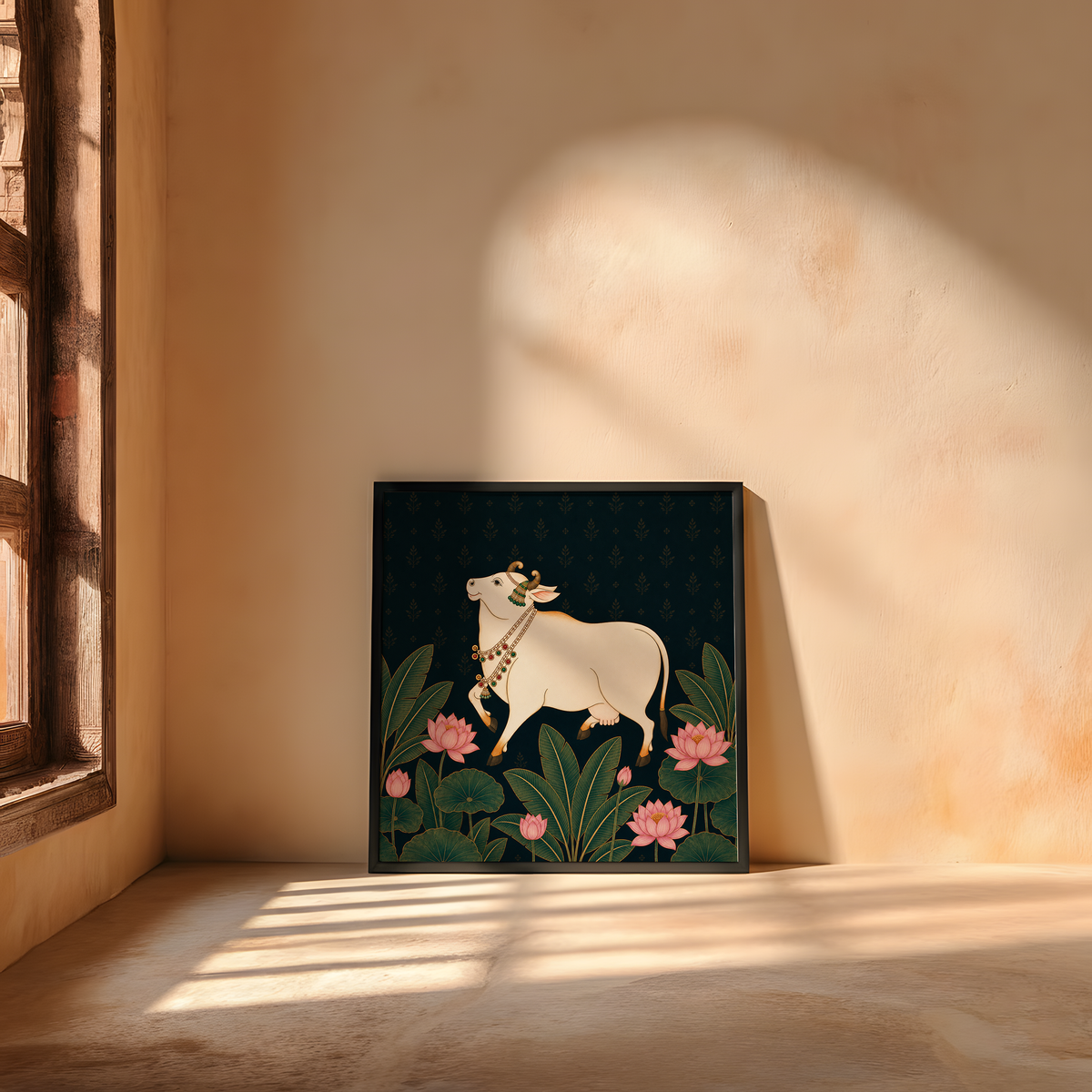 A framed art print featuring a white cow decorated with a floral crown and necklace, walking among green lotus leaves and pink lotus flowers on a dark background, leaning against a warm beige plaster wall in a sunlit room.