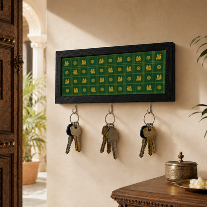 A rectangular black-framed wall key holder with a green grid design and three hanging keys, mounted on a beige wall in a home interior setting.