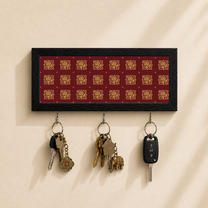 A rectangular black key holder with a red background and repeating gold decorative motifs, mounted on a beige wall. Three metal key rings hang below, holding keys and a car key fob.