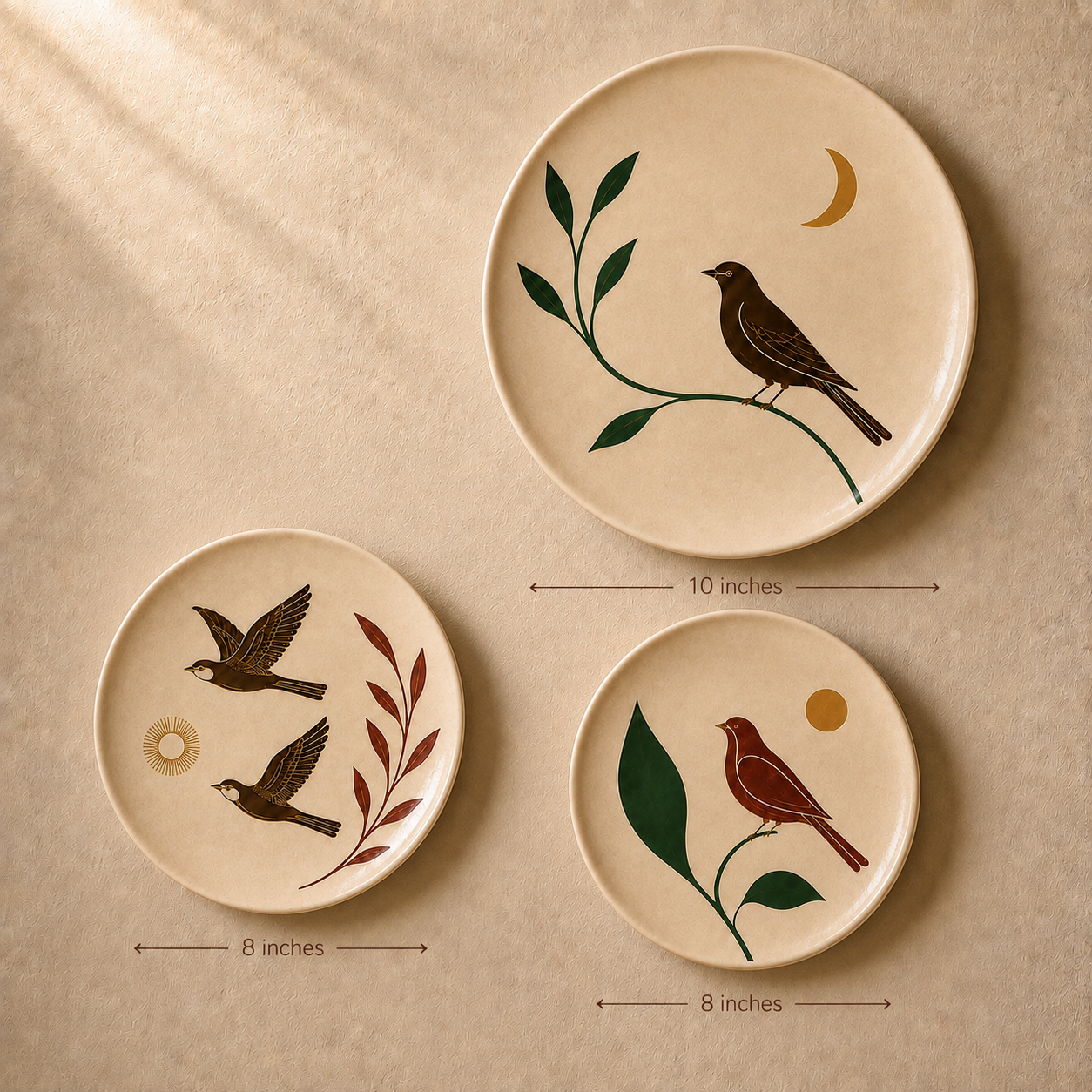Three round ceramic plates with natural beige backgrounds, decorated with hand-painted nature illustrations of birds, leaves, and moons. The plates are arranged on a textured beige surface with soft diagonal shadows, and dimension arrows indicate their sizes: 10 inches, 8 inches, and 8 inches.